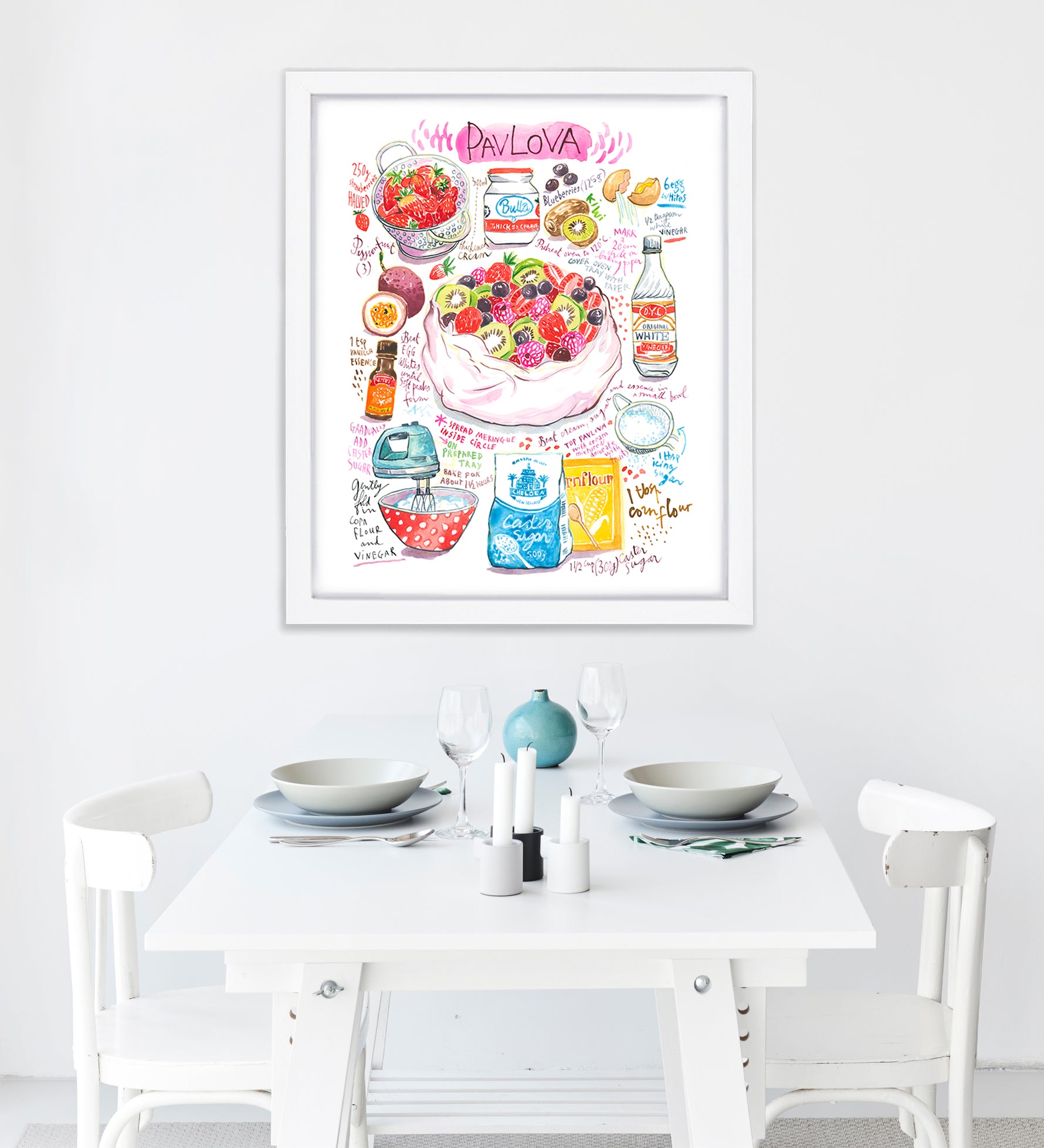 pavlova recipe fine art print in watercolor featuring the ingredients and the finished dish, along with handwritten instructions in English. The framed poster hanging in a dining space.