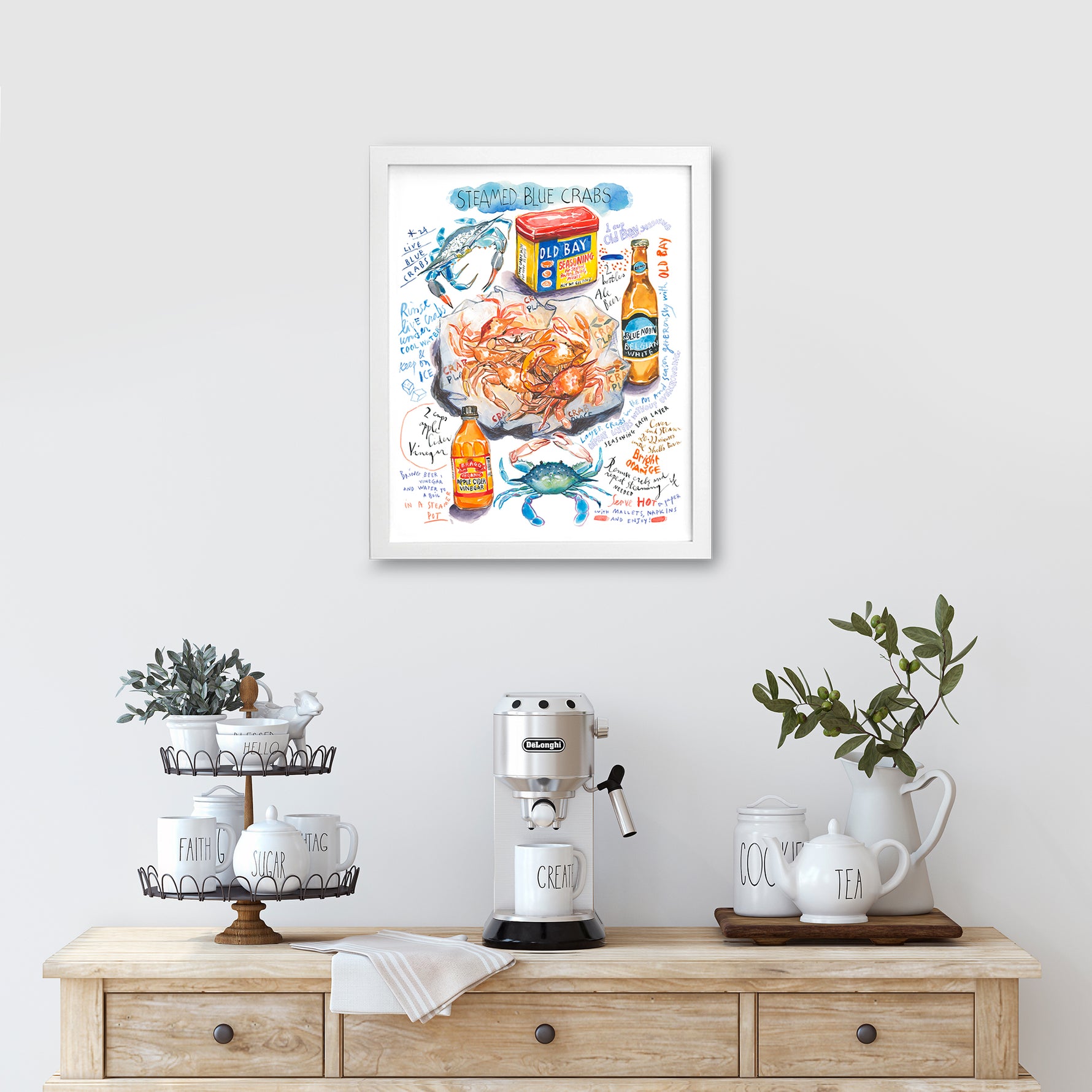 steamed blue crab recipe fine art print in watercolor featuring the ingredients and the finished dish, along with handwritten instructions in English. The framed poster hanging in a kitchen space.