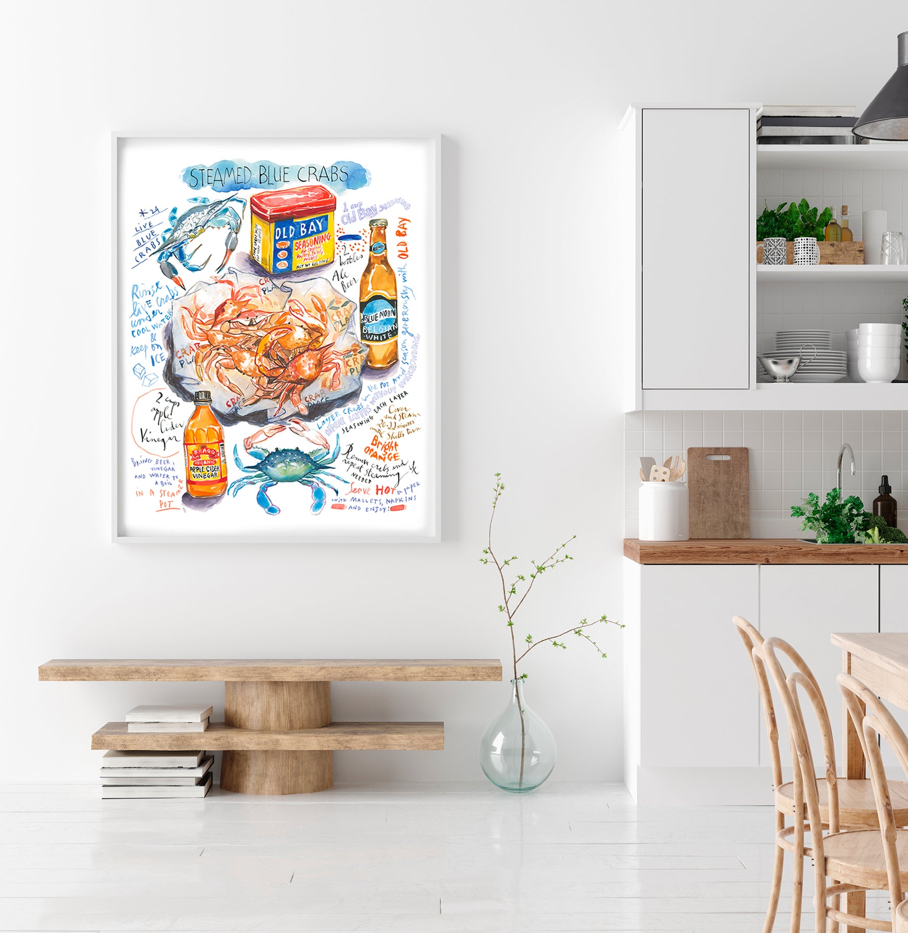 steamed blue crab recipe fine art print in watercolor featuring the ingredients and the finished dish, along with handwritten instructions in English. The framed poster hanging in a dining space.