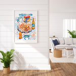 steamed blue crab recipe fine art print in watercolor featuring the ingredients and the finished dish, along with handwritten instructions in English. The framed poster hanging in a dining space.