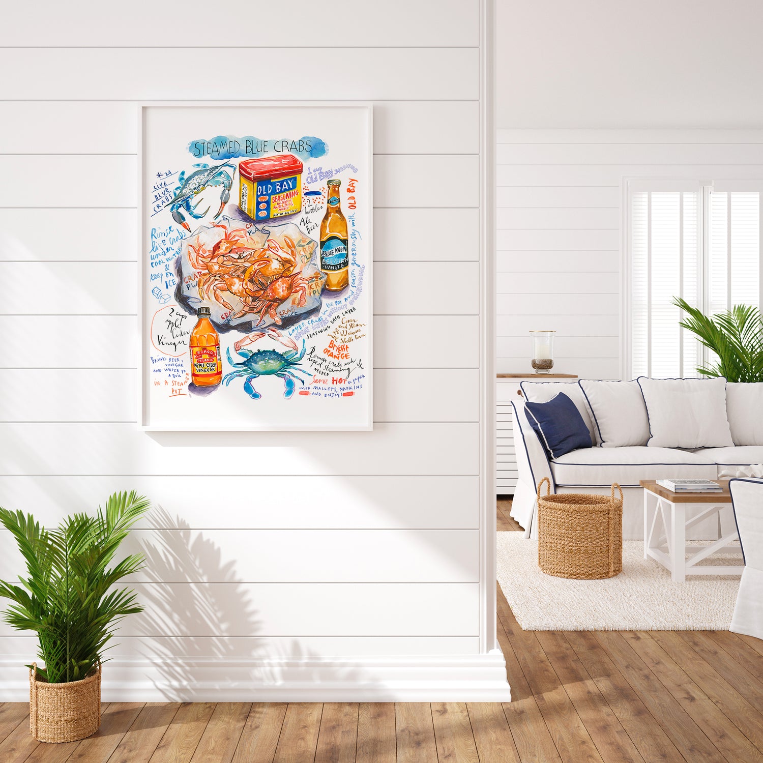 steamed blue crab recipe fine art print in watercolor featuring the ingredients and the finished dish, along with handwritten instructions in English. The framed poster hanging in a dining space.