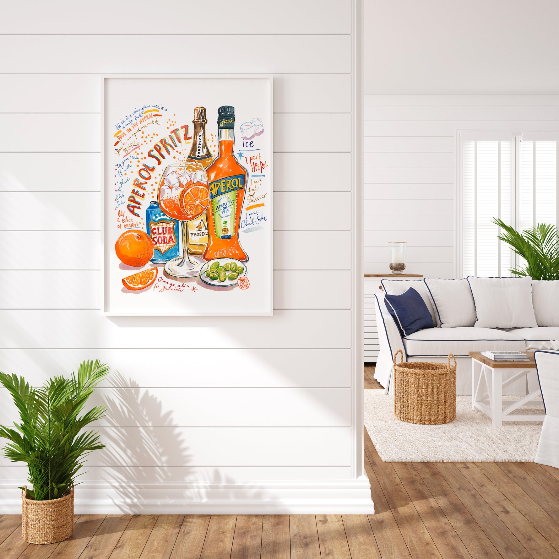 an aperol spritz recipe fine art print in watercolor featuring the ingredients and a glass filled with this cocktail, along with handwritten instructions in English. The framed poster hanging in a home space.
