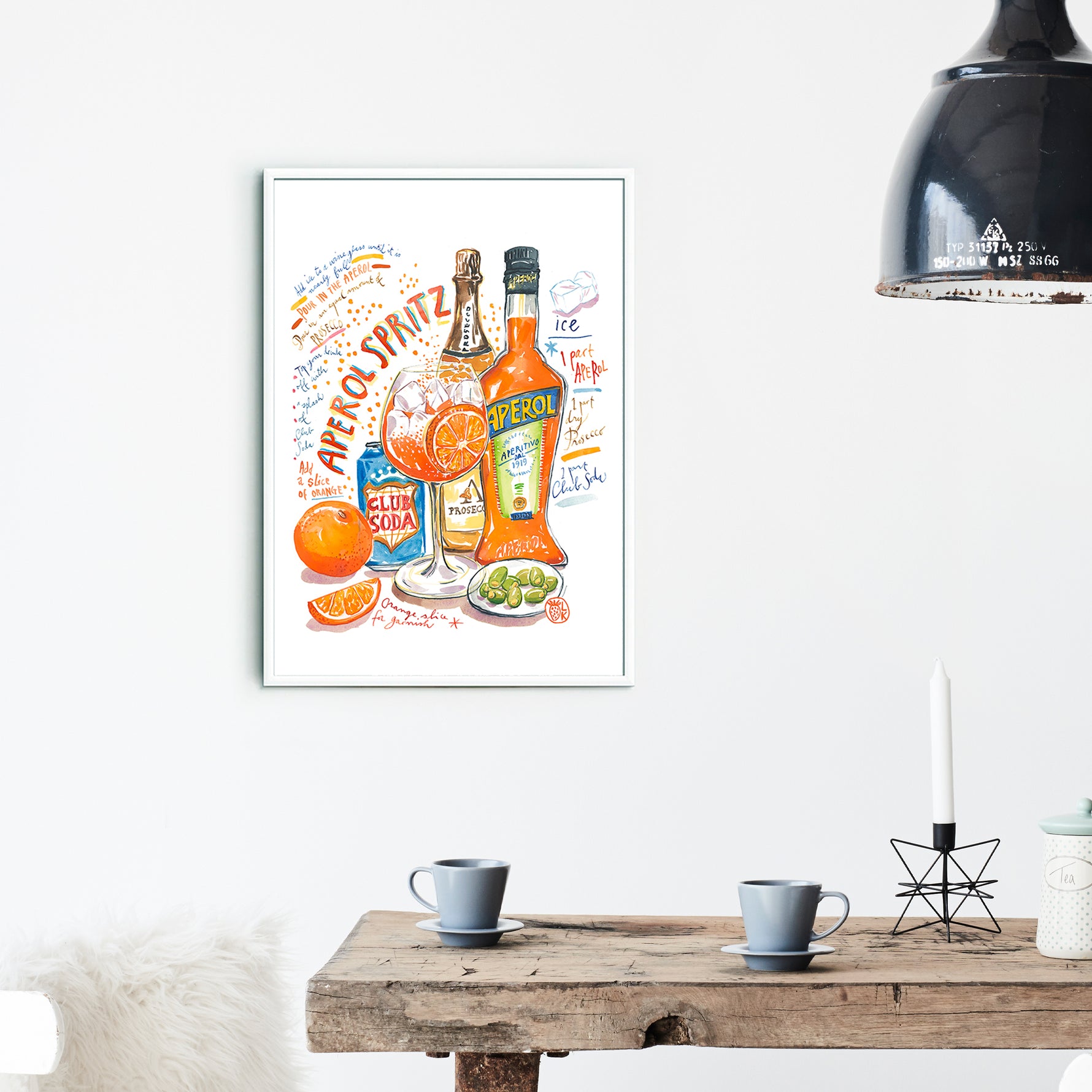 an aperol spritz recipe fine art print in watercolor featuring the ingredients and a glass filled with this cocktail, along with handwritten instructions in English. The framed poster hanging in a dining space.