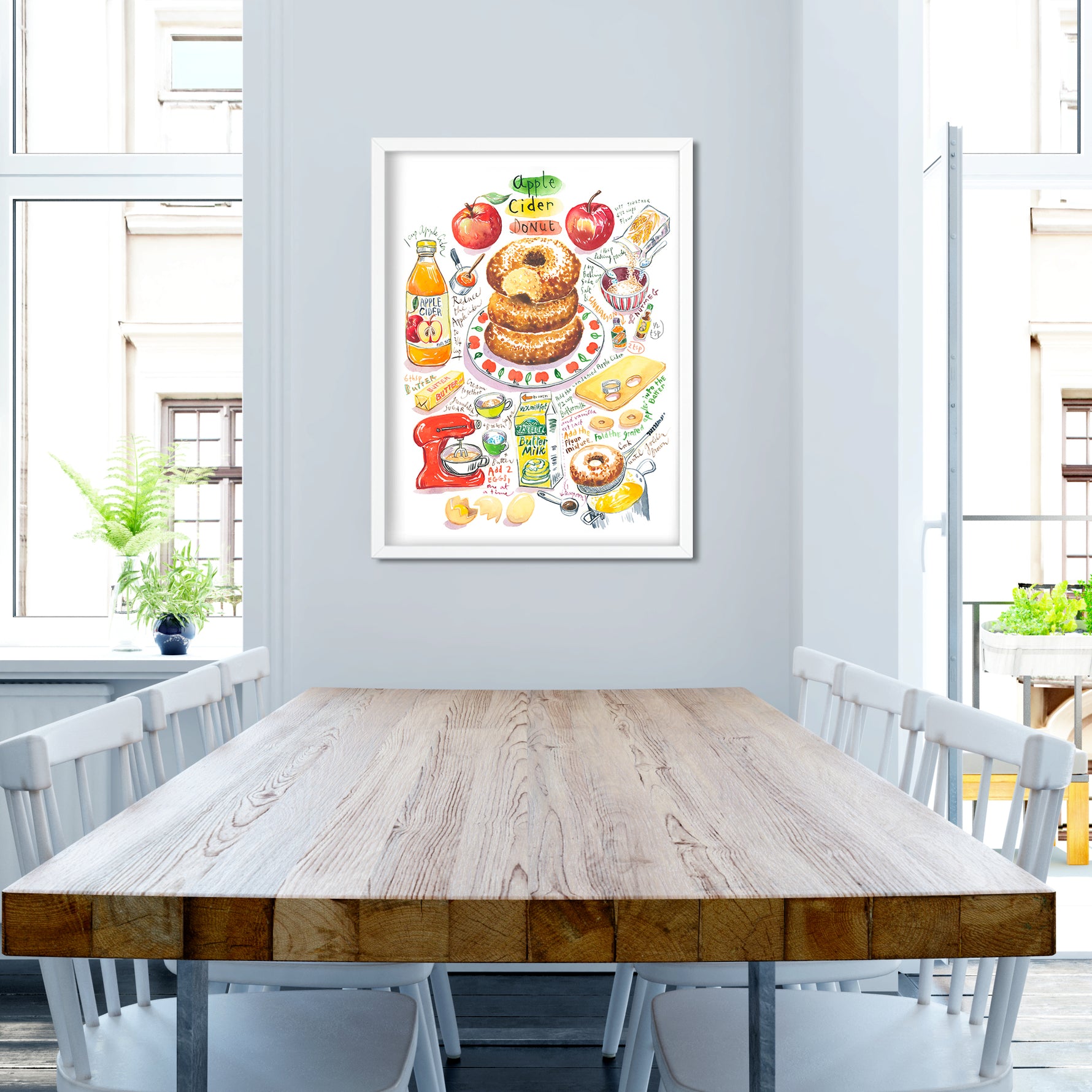 an apple cider donut recipe fine art print in watercolor featuring the ingredients and the finished dessert, along with handwritten instructions in English. The framed poster hanging in a dining space.