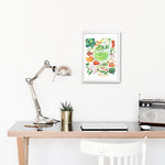 hand painted watercolor print featuring many fresh vegetables and " Framers Market " is hand written in the center of the painting. The print is framed in a working space