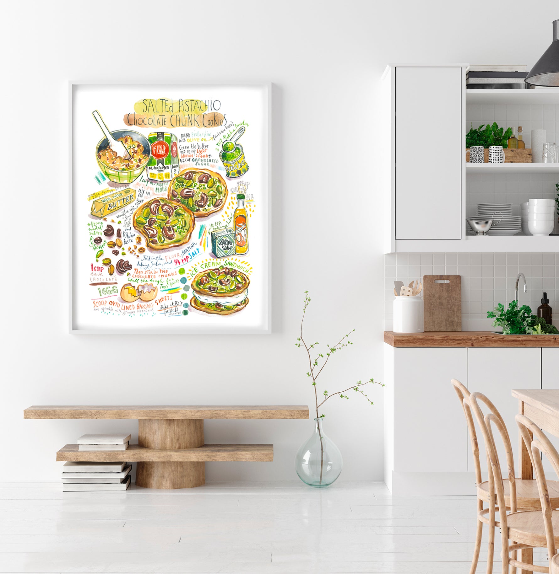 Salted pistachio chocolate chunk cookies recipe fine art print in watercolor featuring the ingredients and two cookies, along with handwritten instructions in English. The framed poster hanging in a dining space.