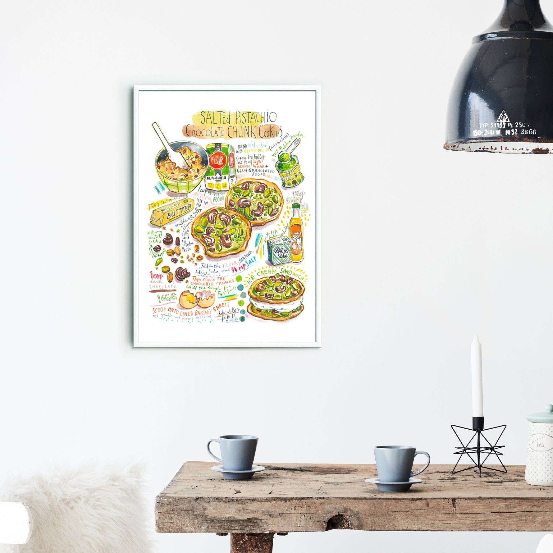 Salted pistachio chocolate chunk cookies recipe fine art print in watercolor featuring the ingredients and two cookies, along with handwritten instructions in English. The framed poster hanging in a dining space.